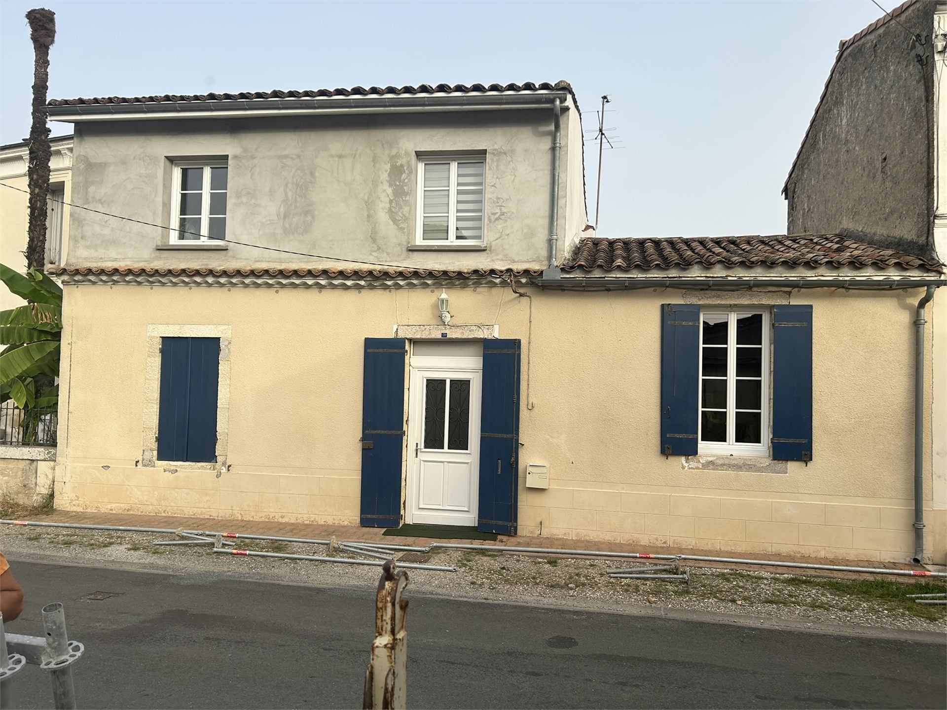 Façade de maison avec enduit dégradé avant restauration, volets bleus
